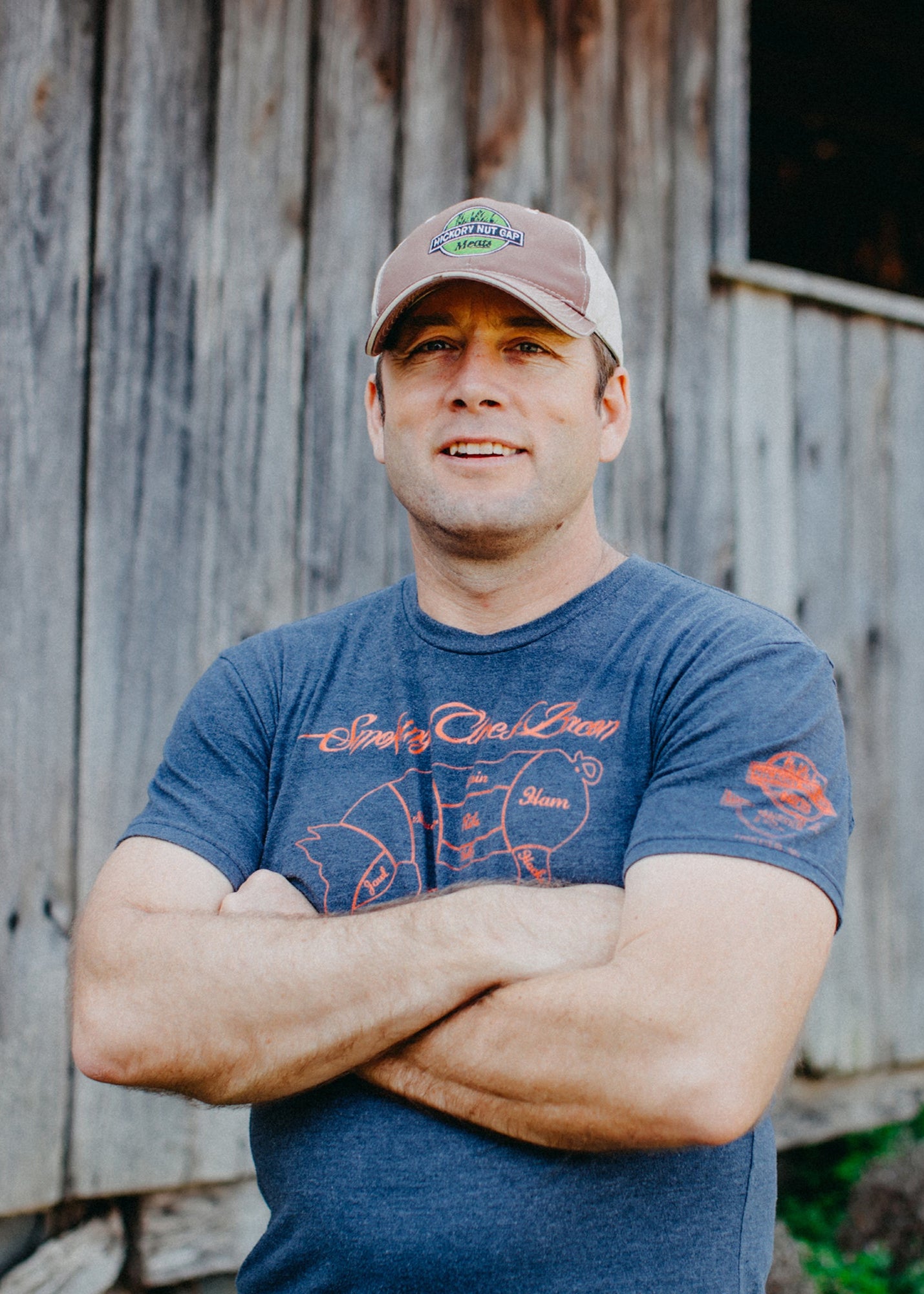 Man wearing a cap and blue t-shirt standing in front of a wooden building