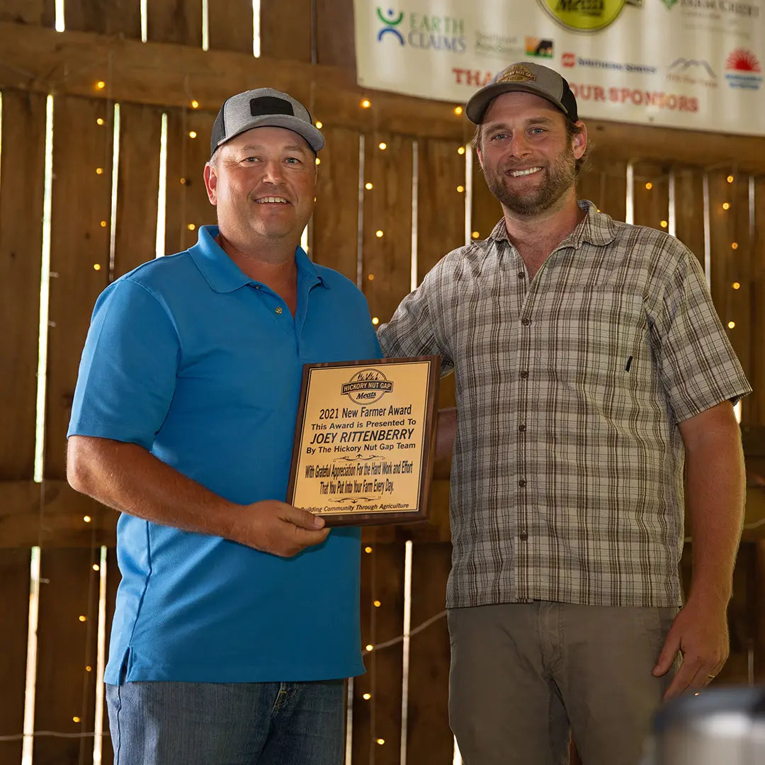 Two men standing in a barn-like setting, one holding an award plaque.